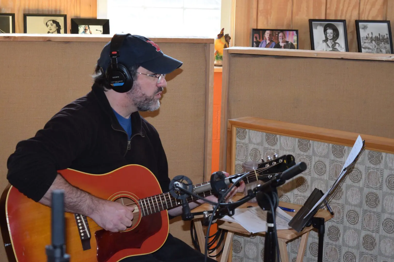 A man playing an acoustic guitar in front of microphones.
