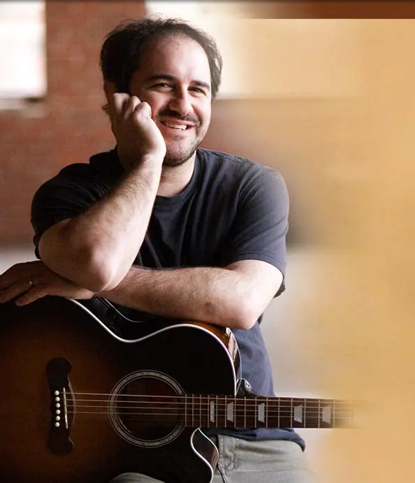 A man sitting in front of an acoustic guitar.