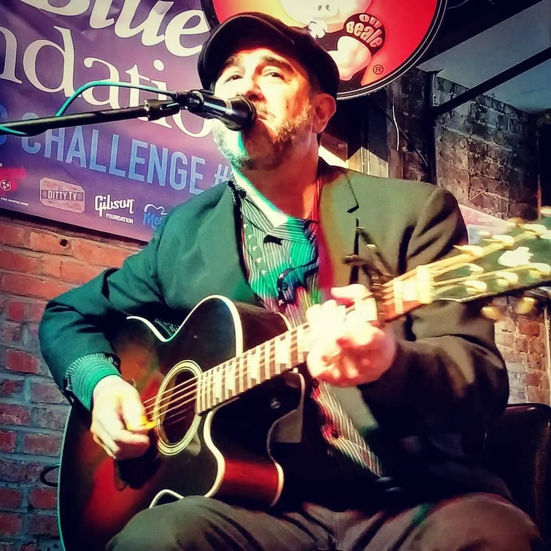 A man playing an instrument while sitting on the floor.