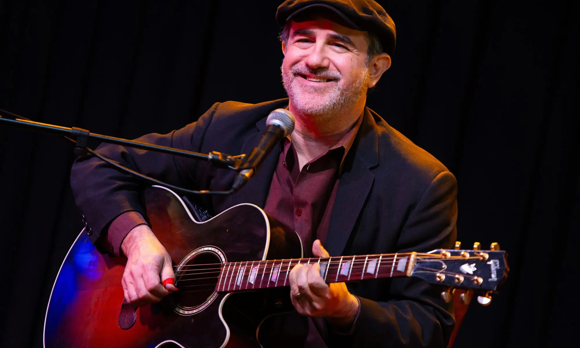 Smiling man playing acoustic guitar on stage.