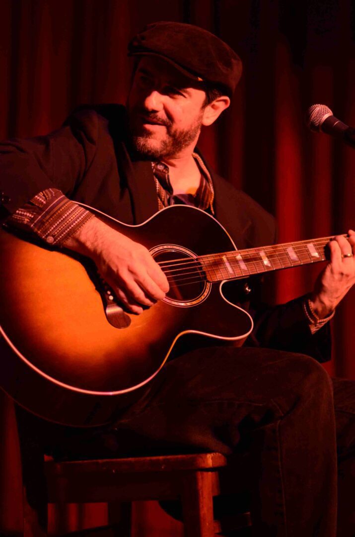 A man sitting down playing an acoustic guitar.